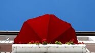 Ein roter Sonnenschirm und rote Geranien sind auf einem Balkon zu sehen., © Sven Hoppe/dpa