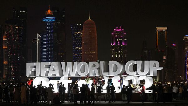 Menschen stehen vor der Eröffnung der WM vor einem beleuchteten Schriftzug «Fifa World Cup Qatar 2022»., © ---/kyodo/dpa