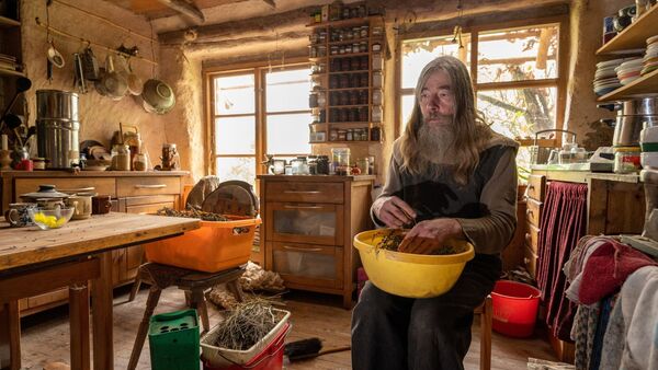 Friedmunt Sonnemann sitzt in der Küche seiner selbstgebauten Lehmhütte., © Harald Tittel/
