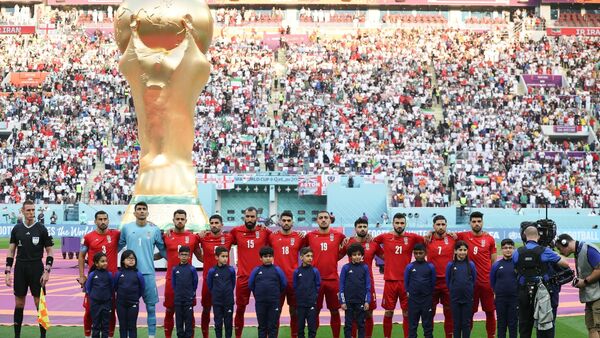 Spieler des Iran stehen beim Abspielen der Nationalhymne vor dem übergroßen Weltpokal im Stadion in Katar., © Han Yan/XinHua/dpa